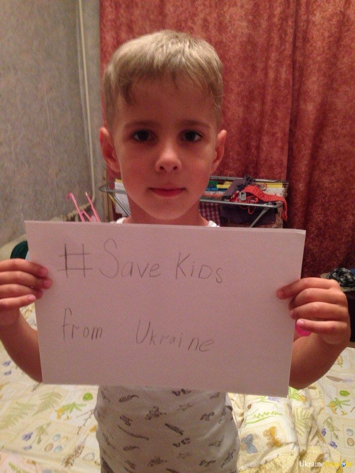 a small boy holding a sign with "#SaveKIds from Ukraine"